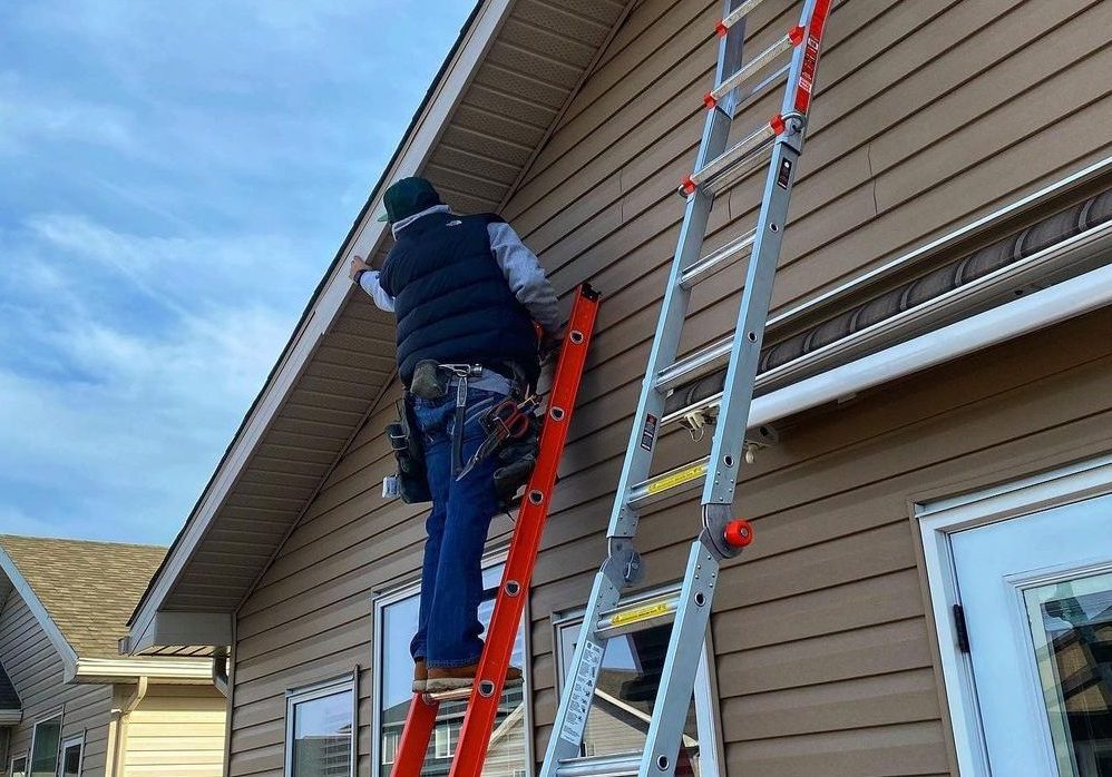 143836291_803181973887817_7292602931144908337_n Construction worker on orange ladder performing maintenance on a residential building's exterior, with a second ladder nearby, showcasing hands-on project execution.